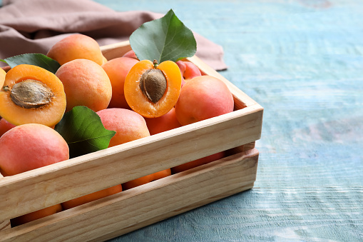 Delicious fresh ripe apricots in crate on blue wooden table, closeup