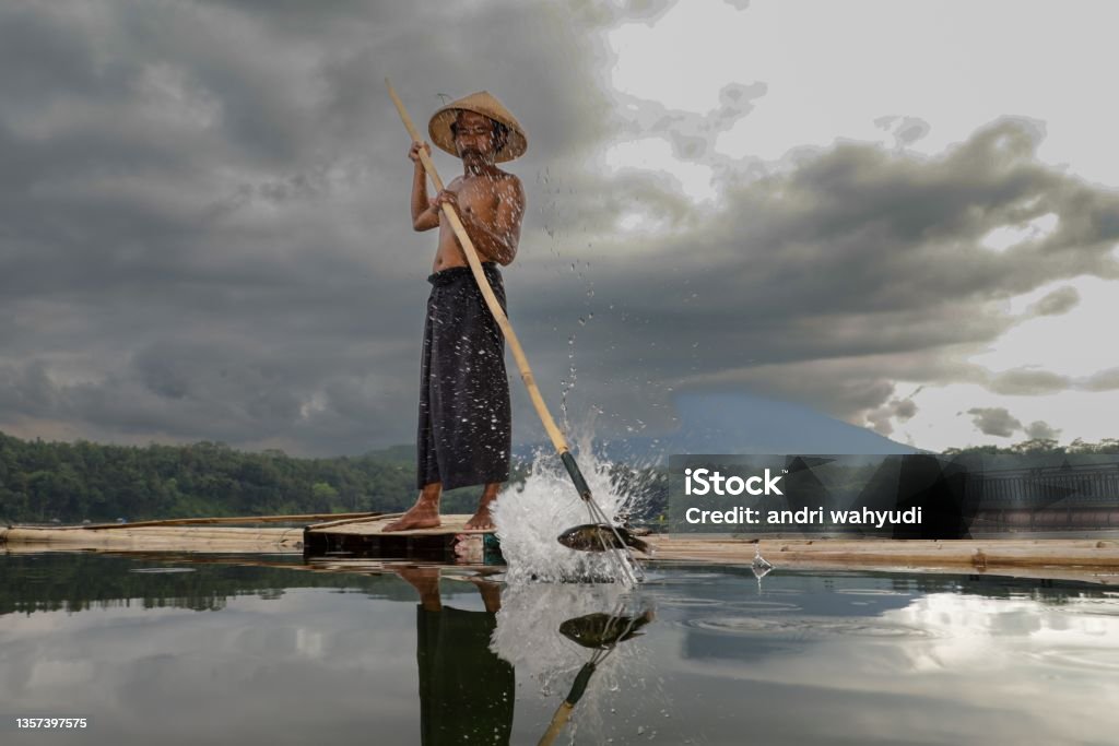 a fisherman, taking fish from the water in the lake using a spear Indonesia Stock Photo
