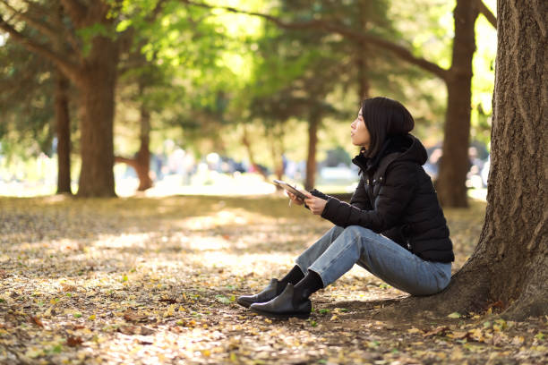 istock Young woman sitting on Autumn leaves and using tablet PC 1357398579