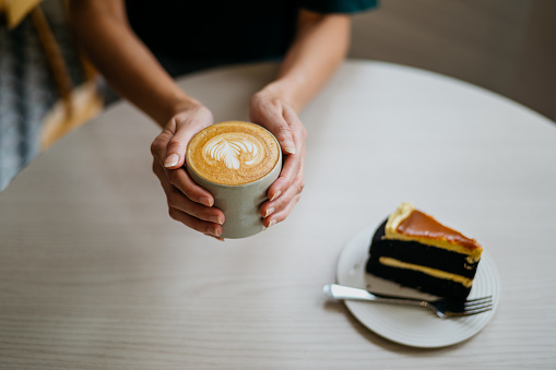 Image of an Asian woman having coffee break with a slice of cake in cafe