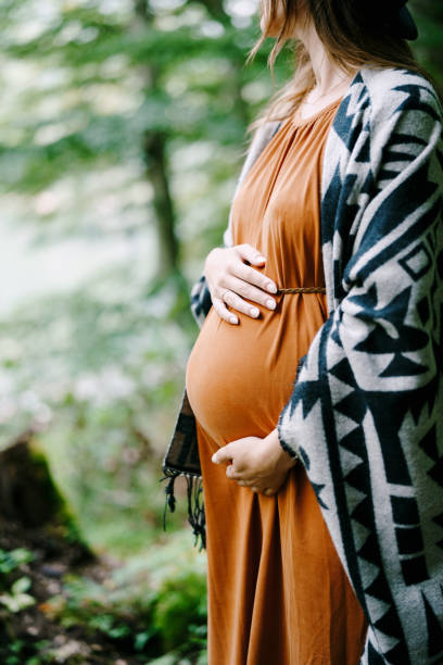 pregnant woman hugs her belly with her hands in the park - dress human pregnancy young women women imagens e fotografias de stock