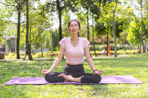 middle aged asian women sitting and meditating in public park with her eyes closed
