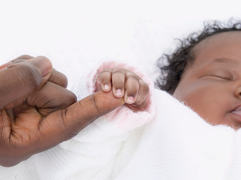 One-month-old baby girl sleeping while holding her father’s hand, photo, white background
