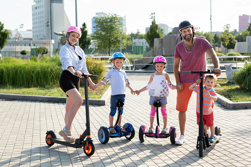Portrait of family with kids on electric scooters and gyro scooter in the Park in the summer.