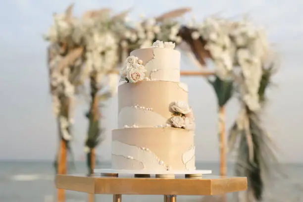 Photo of Wedding cake at a beach wedding on the background of a beautiful arch for an exit ceremony.