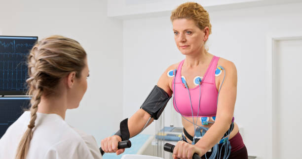 Woman taking a cardiopulmonary stress test in clinic Young female doctor observing the progress of a cardiopulmonary stress test taken by the mature woman riding a bicycle ergometer. stress test stock pictures, royalty-free photos & images