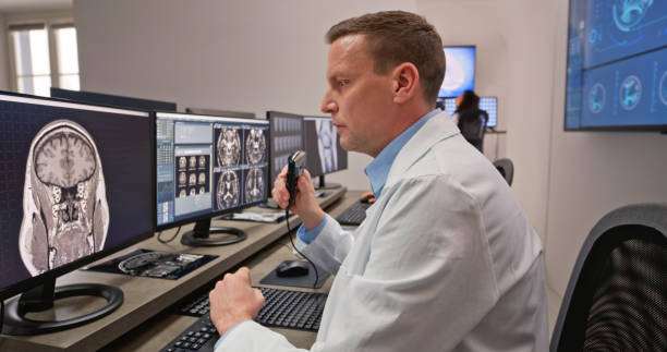 istock Male radiologist speaking into a dictation recorder while looking at MRI scan 1357410980