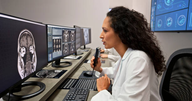 istock Female radiologist speaking into a dictation recorder while looking at MRI scan 1357411085