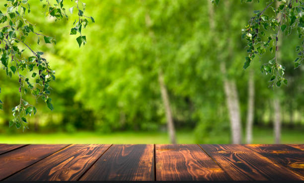 istock Forest wooden table background. Summer sunny meadow with green grass, forest trees background and rustic wooden surface for goods, products, food 1357413580
