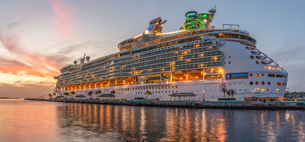Nassau, Bahamas - June 22, 2019: Beautiful panoramic shot of Mariner of the Seas cruise ship docked at Prince George Wharf at sunset. Reflections in the water in the foreground.