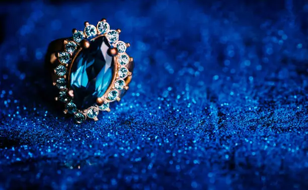 Photo of Closeup of luxury wedding ring in dark blue glitter background.