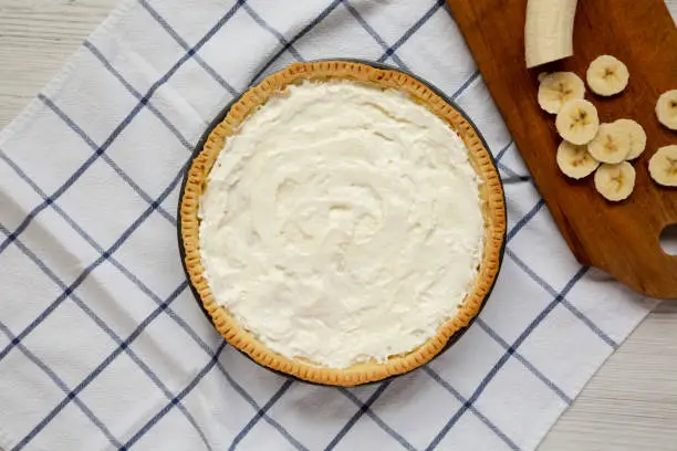 Homemade Tasty Banana Cream Pie on a white wooden surface, top view. Flat lay, overhead, from above. Copy space.