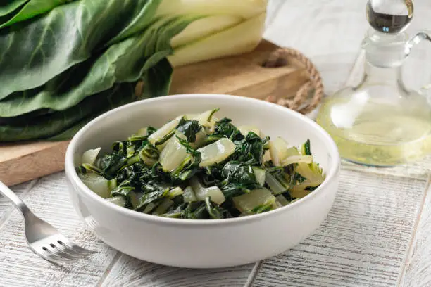 Steamed swiss chard leaves with lemon and olive oil, and fresh uncooked vegetable on background.