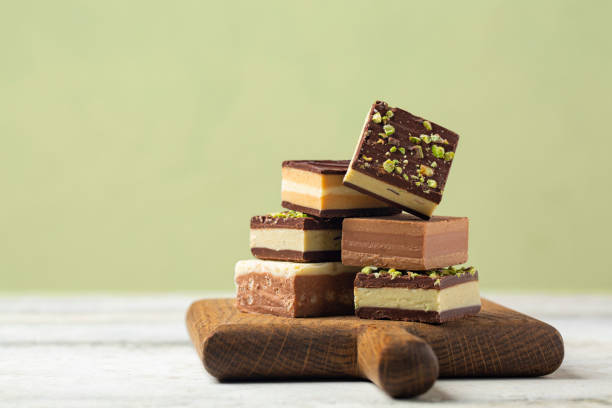Different cremino - italian chocolate,  originally from Piedmont, composed by different layers, made with gianduja chocolate, coffee, pistacchio and hazelnut paste. On light pistacchio color background.