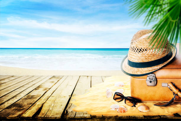 istock Vintage suitcase, sunglasses and hipster hat on sand with seashells with blur seaside background. 1357419940