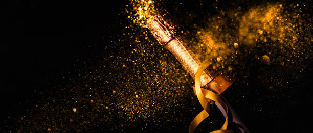 Champagne bottle with gold ribbon on dark background Luxury new year background. Champagne bottle with gold ribbon on dark background with golden bokeh glitter firework. Christmas celebration panoramic design banner. exclusive dinner stock pictures, royalty-free photos & images