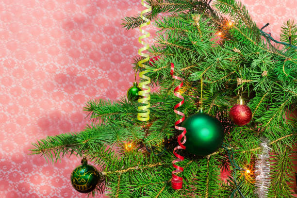Branches of the Christmas tree, decorated with Christmas ornaments and lights on a blurred red background