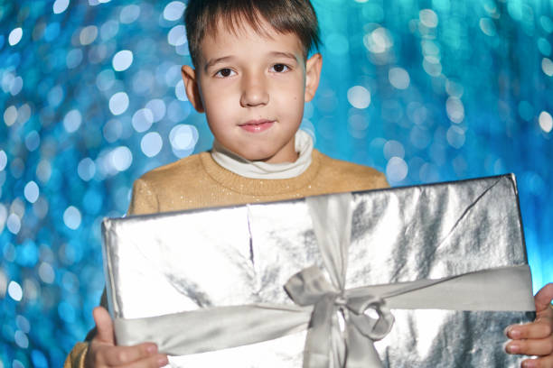 istock Portrait. Nice Elementary Age Boy Is Looking At Camera And Holding Big Gift Box 1357424276