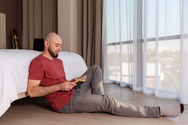 istock A young, bearded, bald man is sitting on the floor at home reading a book. Copy space. The concept of education and reading 1357425821