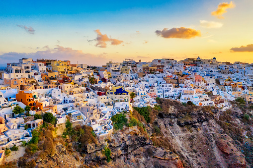 Aerial drone view of famous Oia village with white houses and blue dome churches during sunrise on Santorini island, Aegean sea, Greece