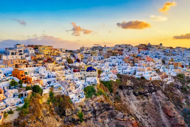 Photo of Aerial drone view of famous Oia village with white houses and blue dome churches during sunrise on Santorini island, Aegean sea, Greece.