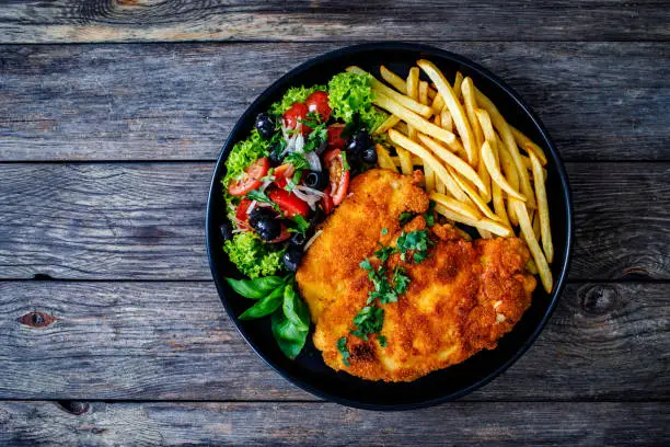 Fried pork chop with French fries and fresh vegetable salad on wooden table