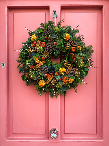 Christmas mood: festive christmasy themed winter natural wreath on a pink wooden door.