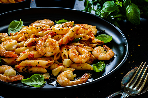 Penne with prawns and garlic in marinara sauce on black wooden table