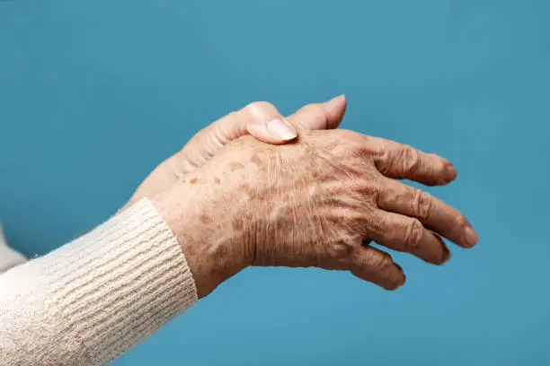 A senior woman is doing a brush massage, experiencing pain. Blue background, hands close-up. The concept of rheumatism and arthritis.