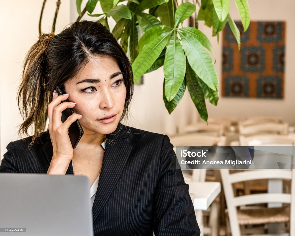 Asian young businesswoman with laptop holding smartphone, female business person calling, telecommunting remote working place Telecommuting Stock Photo