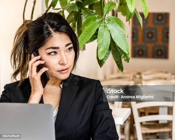 Asian Young Businesswoman With Laptop Holding Smartphone Female Business Person Calling Telecommunting Remote Working Place Stock Photo - Download Image Now