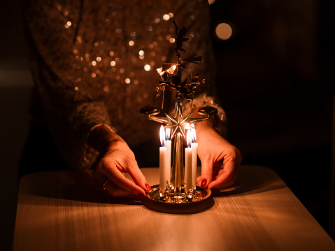 Woman lighting candles on Angel chimes lights for christmas
Photo taken indoors, close up of hands