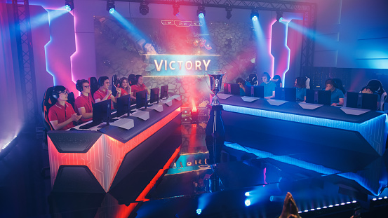 Two Esport Teams of Pro Gamers Play in RPG Strategy Video Game on a Championship Arena, Happy Red Team Wins Round and Celebrates with High-Fives. Big Screen Showing Victory Sign. Cyber Games Event