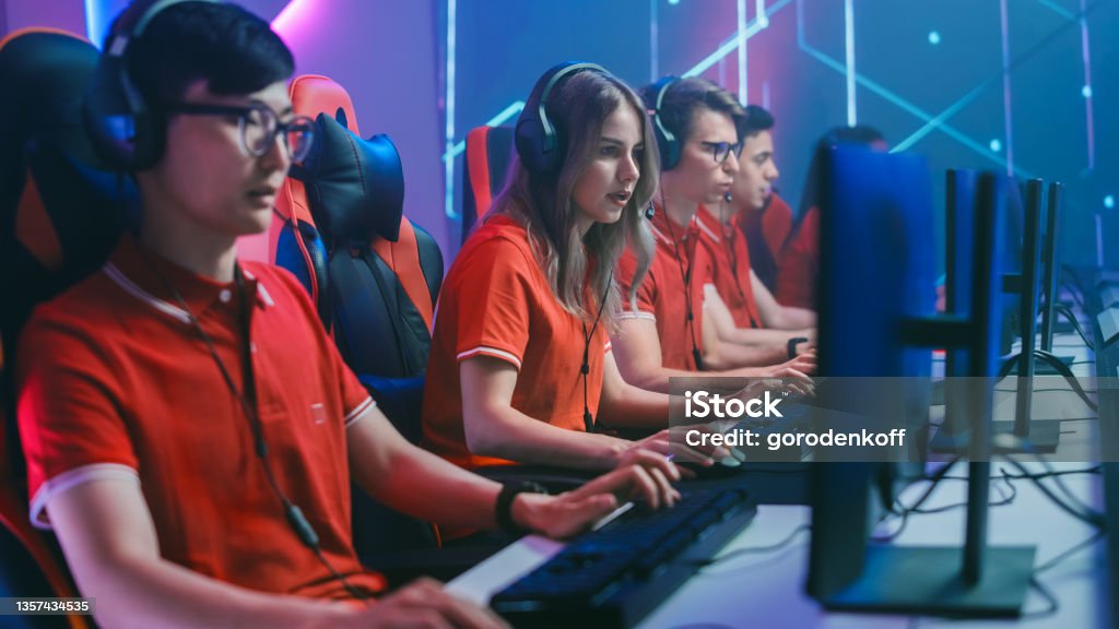 Diverse Esport Team of Pro Gamers Play in Mock-up RPG Strategy Video Game on a Championship. Stylish Neon Cyber Games Arena. Online Broadcasting of Tournament Event. Side View Shot eSports Stock Photo