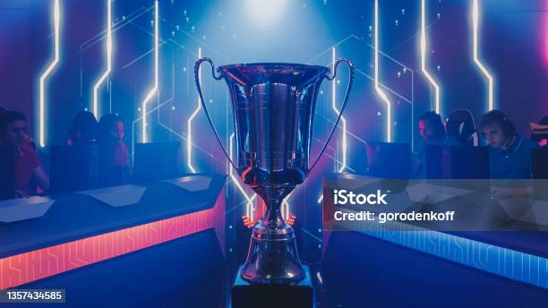 Two Esport Teams Of Pro Gamers Play To Compete In Video Game On A Championship Stylish Neon Cyber Games Online Streaming Tournament Arena With Trophy In The Center Stock Photo - Download Image Now