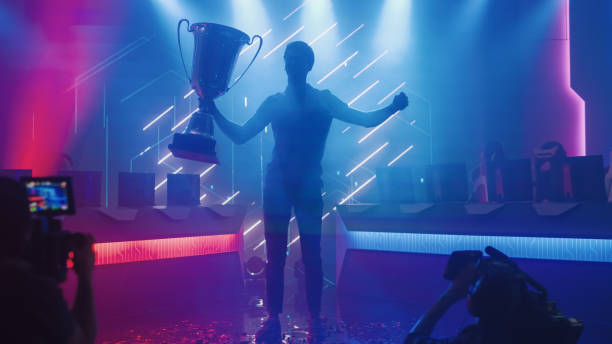 professional video games player tournament winner celebrates victory cheering and holding trophy. big stylish neon bright championship arena doing pro computer gaming event with online streaming - esport audience bildbanksfoton och bilder