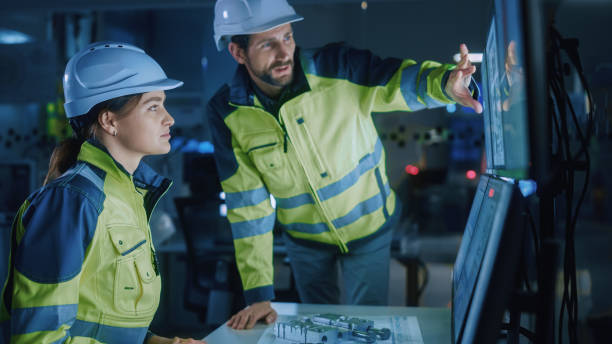 istock Industry 4.0 Modern Factory: Project Engineer Talks to Female Operator who Controls Facility Production Line, Uses Computer with Screens Showing AI, Machine Learning Enhanced Assembly Process 1357436555