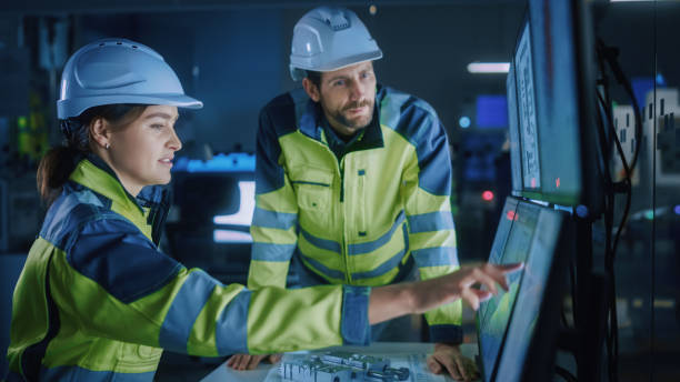 istock Industry 4.0 Modern Factory: Project Engineer Talks to Female Operator who Controls Facility Production Line, Uses Computer with Screens Showing AI, Machine Learning Enhanced Assembly Process 1357436566