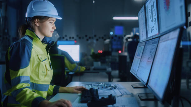istock Industry 4.0 Modern Factory: Female Facility Operator Controls Workshop Production Line, Uses Computer with Screens Showing Complex UI of Machine Operation Processes, Controllers, Machinery Blueprints 1357436572
