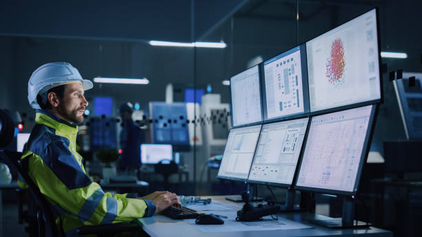 istock Industry 4.0 Modern Factory: Facility Operator Controls Workshop Production Line, Uses Computer with Screens Showing Complex UI of Machine Operation Processes, Controllers, Machinery Blueprints 1357436576