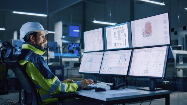 istock Industry 4.0 Modern Factory: Facility Operator Controls Workshop Production Line, Uses Computer with Screens Showing Complex UI of Machine Operation Processes, Controllers, Machinery Blueprints 1357436603