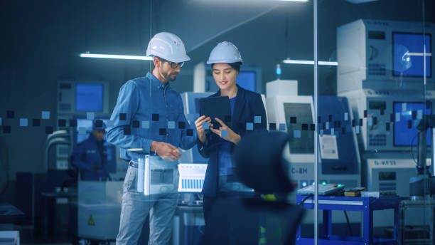 istock Modern Factory: Female Project Manager, Male Engineer Standing in High Tech Development Facility, Talking and Using Tablet Computer. Contemporary Facility with CNC Machinery, Robot Arm Production Line 1357436654