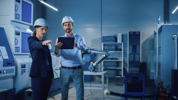 istock Portrait of Two Professional Engineers Use Industrial Digital Tablet to Work with Augmented Reality. Great Template Shot for Augmented Reality. Factory Workshop with CNC Machinery. 1357436659