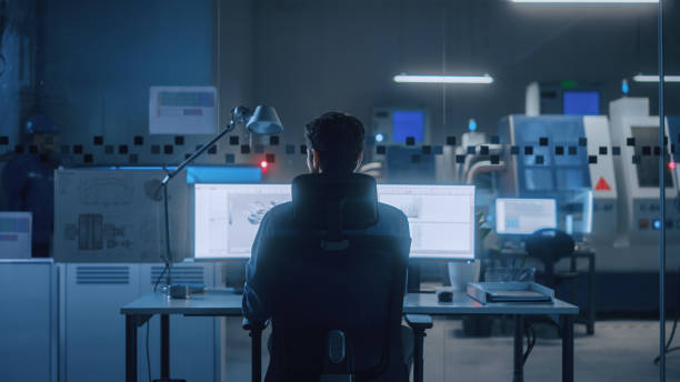 istock Industrial Engineer Solving Problems, Working on a Personal Computer, Two Monitor Screens Show CAD Software with 3D Prototype of Eco-Friendly Electric Engine Concept. Back View Shot 1357436756