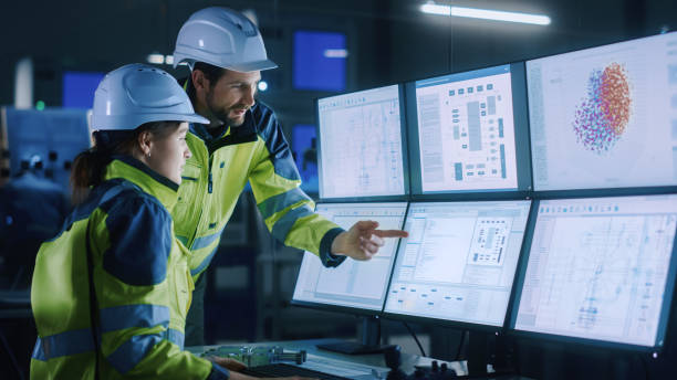 istock Industry 4.0 Modern Factory: Chief Project Manager Talks to Female Engineer, She Points at Computer Screens Showing Complex Industrial Electronics Design Blueprints, They Have Find Problem Solution 1357436778