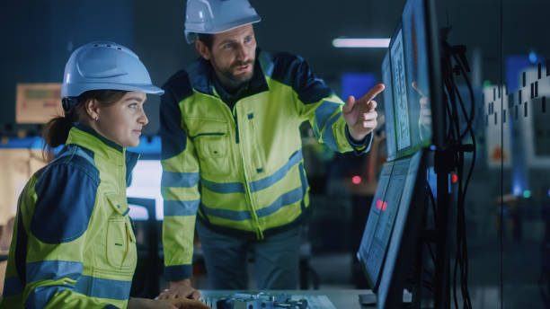 istock Industry 4.0 Modern Factory: Project Engineer Talks to Female Operator who Controls Facility Production Line, Uses Computer with Screens Showing AI, Machine Learning Enhanced Assembly Process 1357436820