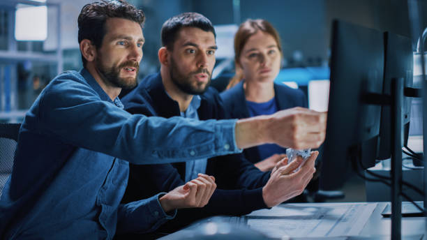 istock Industry 4.0 Modern Factory: Team of Innovative Industrial Engineers Use Computer and 3D Printer to Build Complex Component. Group of Scientists Use High-Tech Machinery for Futuristic Design 1357436821