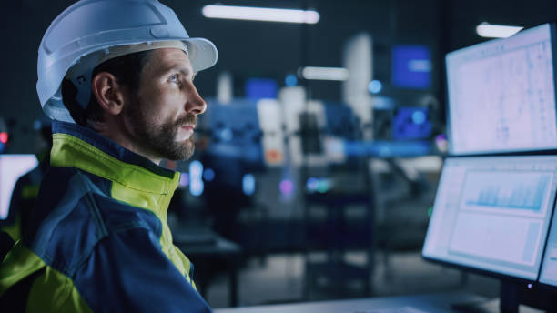 Industry 4.0 Modern Factory: Portrait of Facility Operator Controls Workshop Production Line, Uses Computer with Screens Showing Complex UI of Machine Operation Processes, Controllers industria 4.0 fábrica moderna: retrato de la línea de producción del taller de controles del operador de la instalación, utiliza el ordenador con pantallas que muestran la interfaz de usuario compleja de los procesos de operación de la máquina, contr