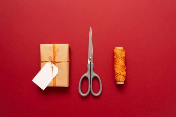 istock Kraft gift box with orange thread, scissors and labels for inscriptions on a red background. 1357441271