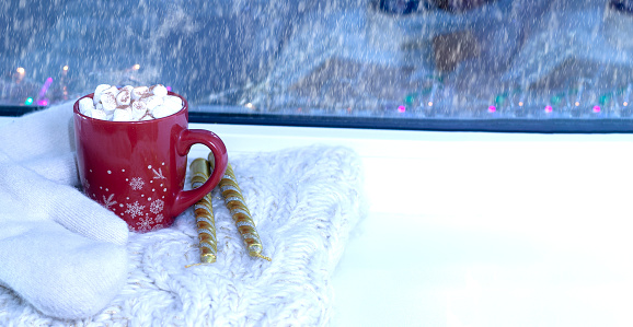 A Christmas red mug in the background with mittens and candles. High quality photo